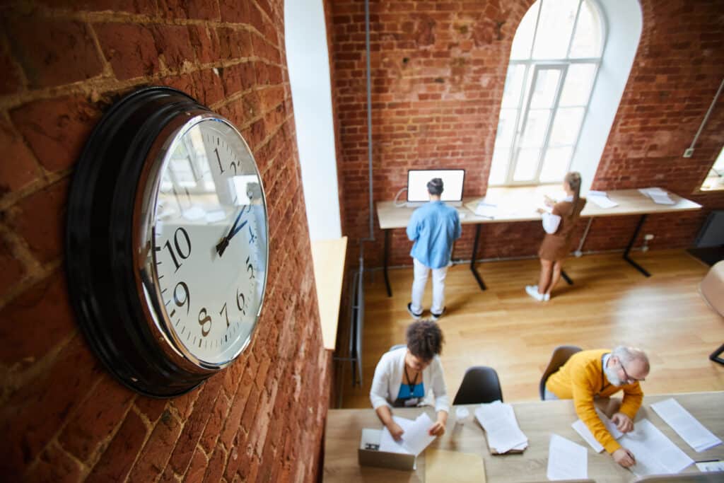 time to market concept with Clock on red brick wall of modern office and colleagues working