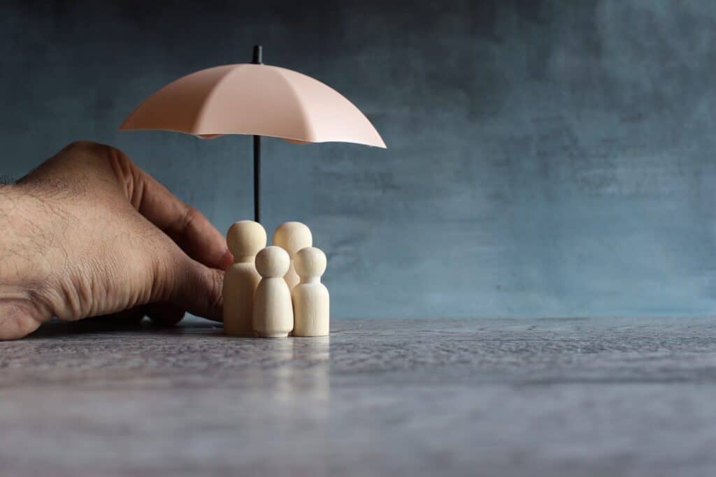 Family safety and protection concept with umbrella and wooden dolls.