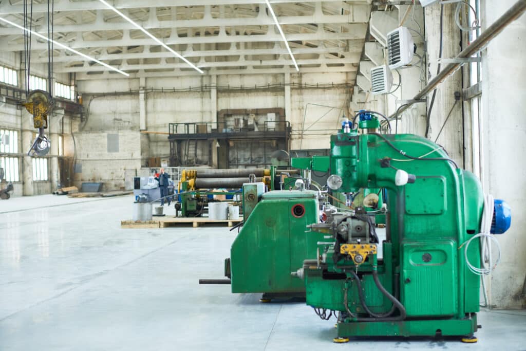 Green drilling machine and industrial equipment in a bright, spacious workshop.