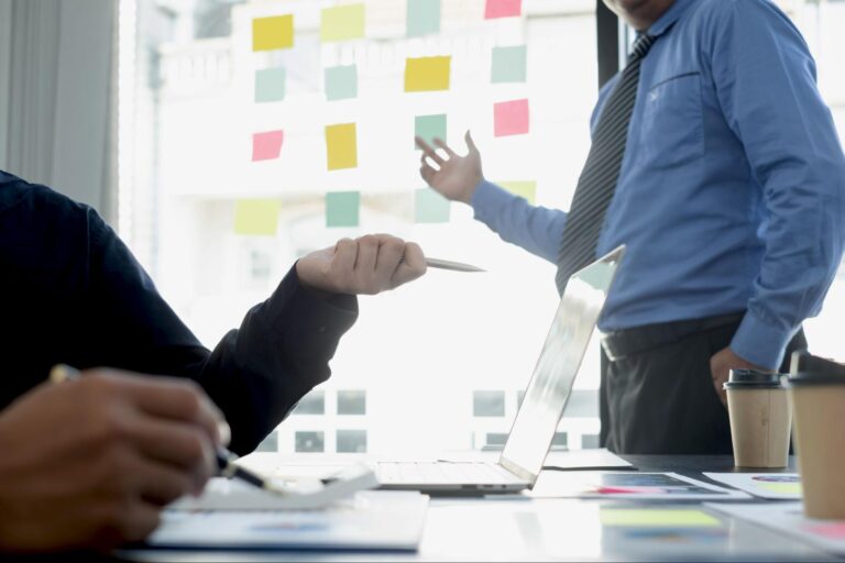 Team brainstorming with sticky notes and laptops in a dynamic meeting setting.
