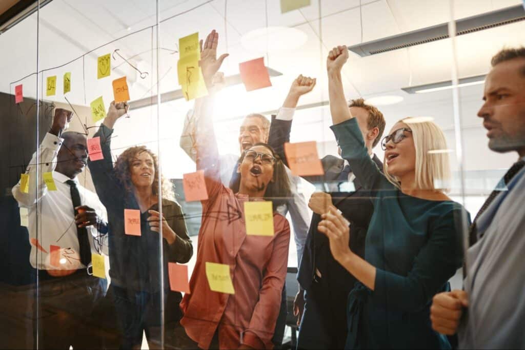 Team members celebrate collaboration with sticky notes and enthusiastic gestures.